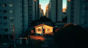 Casa simples em São Paulo cercada por prédios altos ao entardecer, representando o contraste urbano e a luta por regularização fundiária por meio do usucapião extrajudicial gratuito